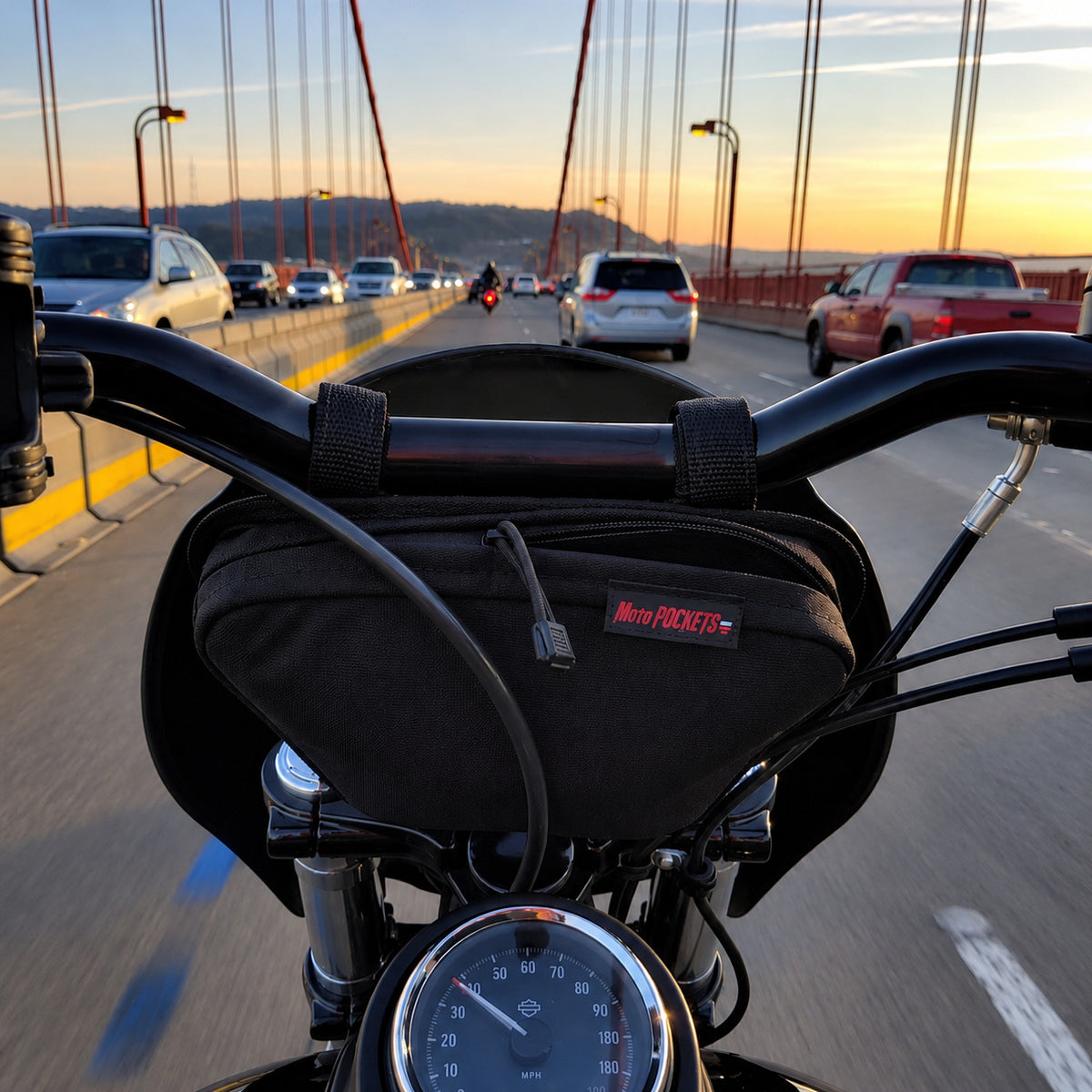 Black Moto Pockets OG T-Bar motorcycle handlebar bag mounted on Harley-Davidson handlebars while crossing a suspension bridge, showing the adjustable mounting straps and compact storage design.