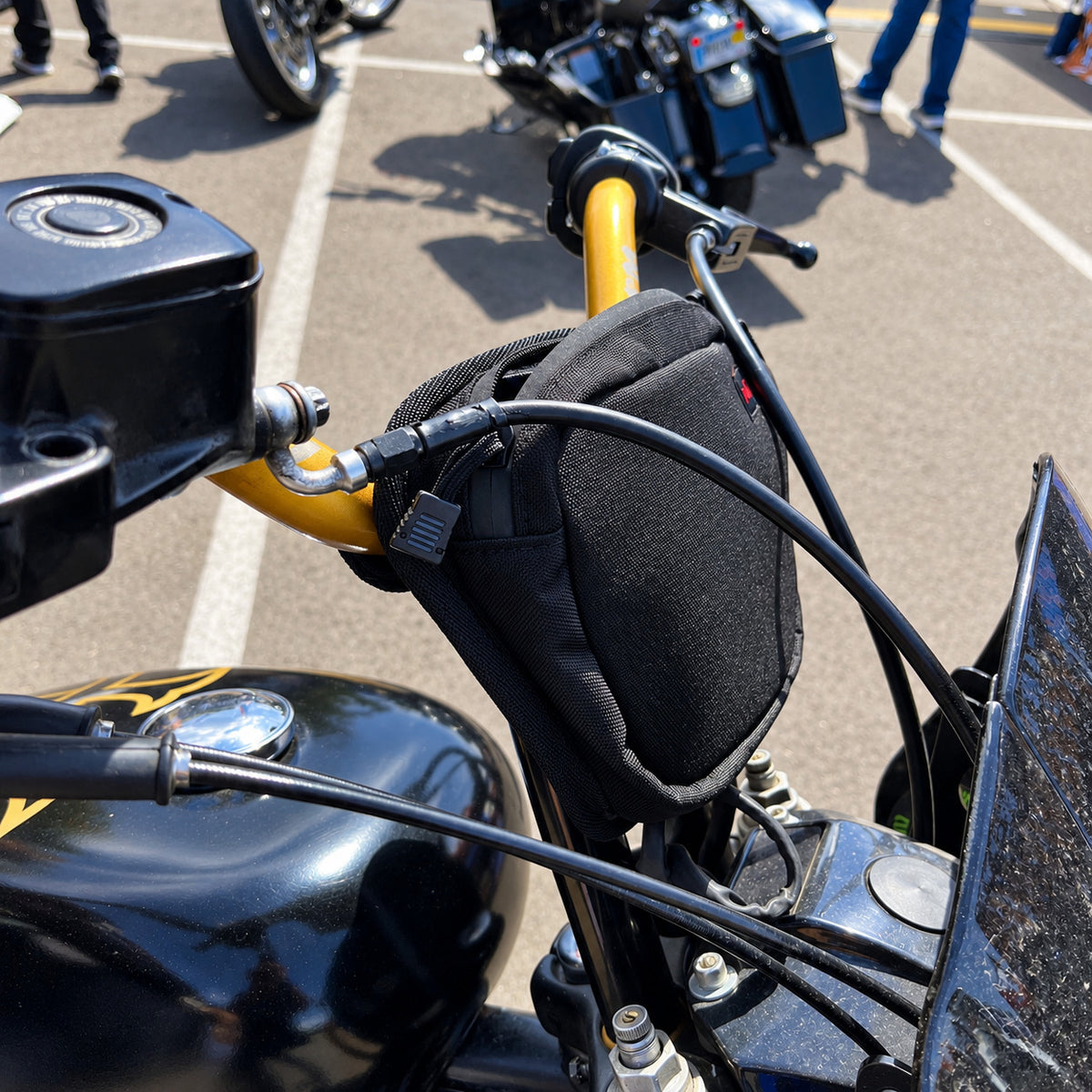 Black Moto Pockets OG T-Bar motorcycle handlebar bag mounted on gold handlebars, showing its compact tapered design, secure mounting position, and easy-access zippered storage.